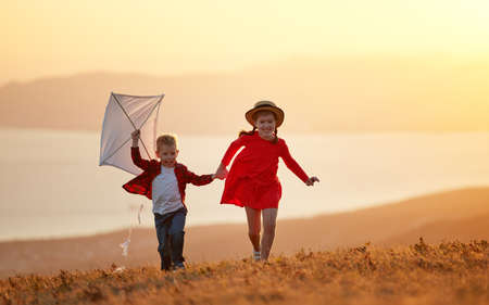 happy kids sister and brother launches a kite at sunset on nature outdoorsの写真素材