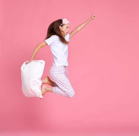 Side view of energetic female in pajama holding pillow and clenching fist while jumping and yelling...