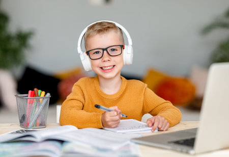 Happy child boy in headphones smiling and looking at camera while making video call to teacher...