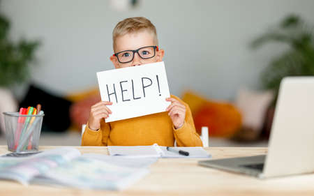 tortured unhappy tired child a boy student holds a sign HELP while doing homework at homeの写真素材
