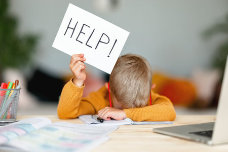 tortured unhappy tired child a boy student holds a sign HELP while doing homework at home