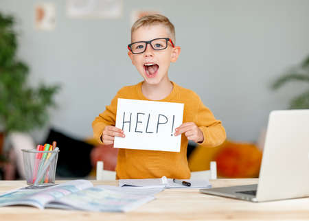 tortured unhappy tired child a boy student holds a sign HELP while doing homework at homeの写真素材