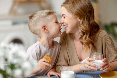 Optimistic woman and boy with milk and cookie smiling and touching noses while having breakfast togetherの写真素材