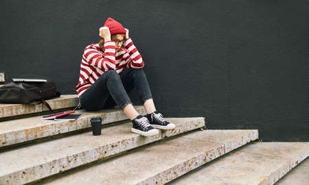 Stressed out student girl sitting outside with hands holding head, having stress before exam or worrying about university tests while sitting in stylish outfit on concrete stairs outdoorsの写真素材