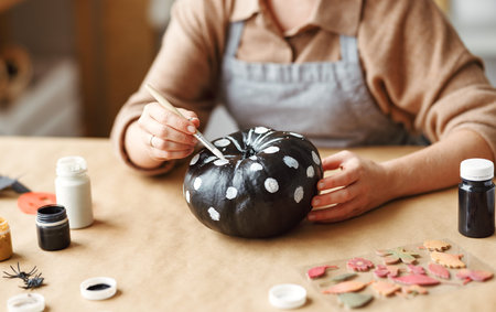 Cropped shot of woman in apron painting Halloween pumpkin with paint brush in handの写真素材