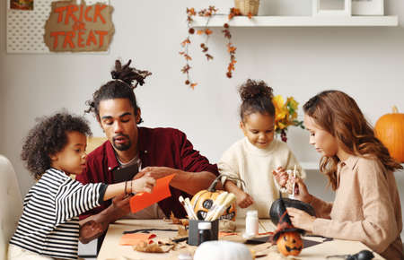 Young joyful african american family mother, father and two kids preparing for Halloween at homeの写真素材