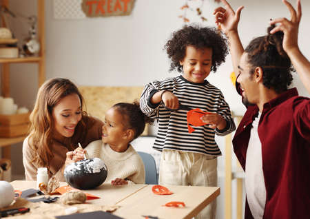 Young joyful african american family mother, father and two kids preparing for Halloween at homeの写真素材