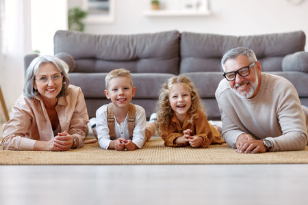 Beautiful cheerful family two cute little kids lying on floor with positive senior grandparents while playing together in living room at home, happy children enjoying time with grandma and grandpaの写真素材