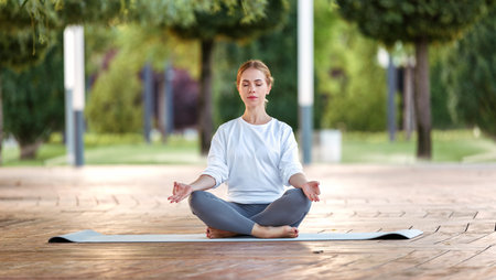 Calm happy young woman sitting in lotus pose on mat during morning ...