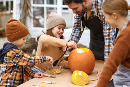 Happy young family carving pumpkins in backyard, children making jack-o-lantern with parentsの写真素材