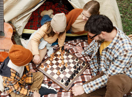 Happy smiling family playing chess game at campsite during camping trip in natureの写真素材