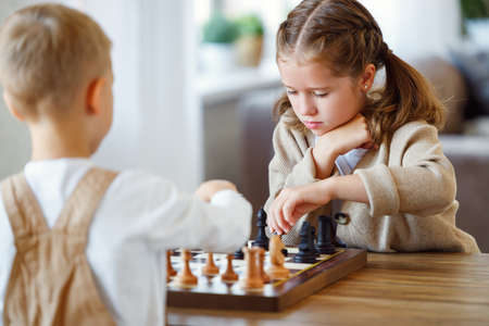 Focused children playing chess game at home while sitting in living room at table with chessboardの写真素材