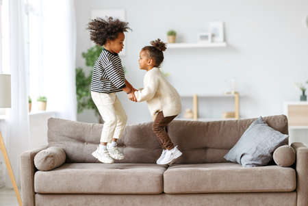 Happy energetic african american children jumping on sofaの写真素材
