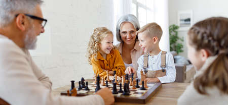 Children brother and sister playing chess while sitting in living room with senior grandparentsの写真素材