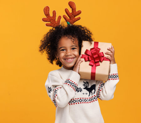 Christmas holidays. Happy little african american boy wearing red deer antlers with xmas gift boxの写真素材