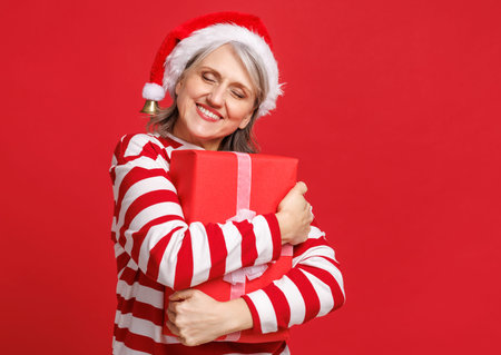 Happy senior woman hugging xmas gift box with closed eyes while celebrating Christmas and New Year