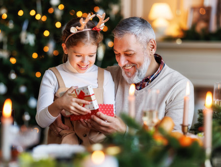 Grandfather with excited girl granddaughter unpacking Christmas gift box near decorated xmas treeの写真素材