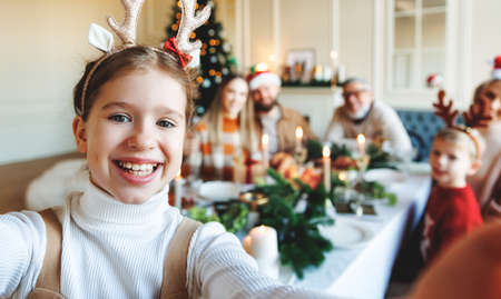 Happy little girl in reindeer antlers taking selfie of large family during Christmas celebrationの写真素材