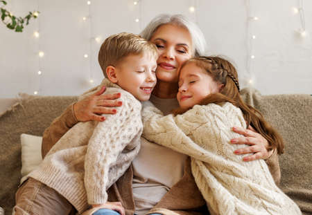Loving senior grandmother hugging cute happy grandchildren during winter holidays at homeの写真素材