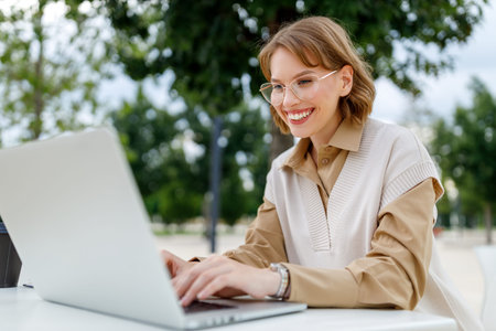 Lovely student girl in glasses sitting with laptop outside on terrace