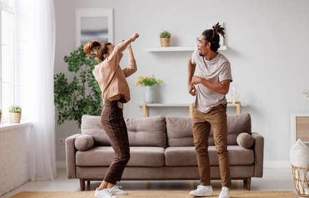 Young overjoyed african american family couple dancing to music on sofa at homeの写真素材
