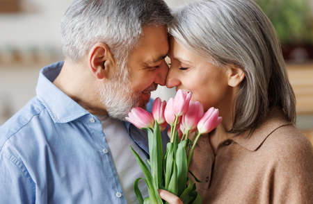 Elderly couple in love hugging on Valentines day. A loving husband gives his wife a bouquet of tulipの写真素材