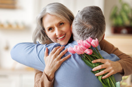 Happy senior woman receiving bouquet of spring flowers tulips from husband on Womens Day at homeの写真素材