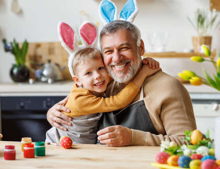 Happy family loving grandfather and cute little boy grandson embracing while painting Easter eggsの写真素材