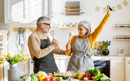 Joyful elderly couple have fun dancing and singing while cooking together in kitchenの写真素材