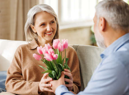 Happy senior woman getting romantic present bouquet of tulips from loving husband on Valentines Dayの写真素材