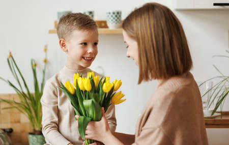 Young woman mother with flower bouquet embracing son while getting congratulations on Mothers dayの写真素材