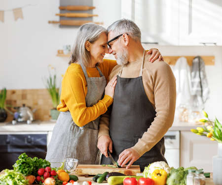 Happy elderly family couple wife and husband embracing while cooking vegetarian food togetherの写真素材