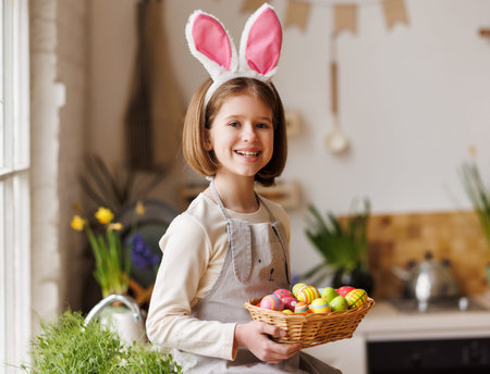 Cute happy little girl wearing plush bunny ears holding Easter basket in kitchen