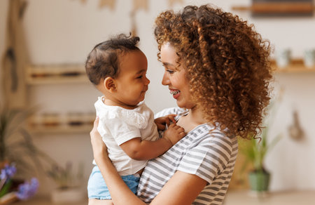 Happy, cheerful ethnic mom holds a laughing baby daughter in her arms.