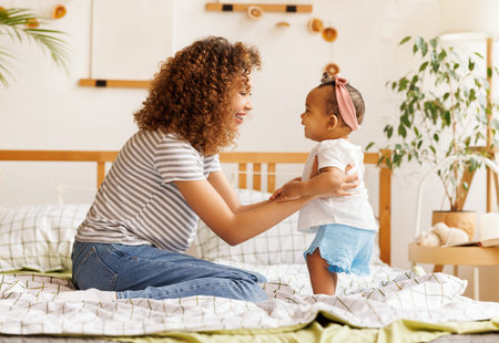 happy african american mother playing with laughing baby daughter in bed