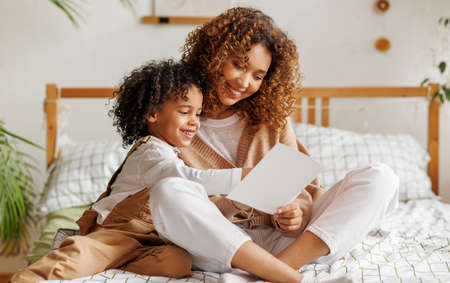 Cute little son giving his mom greeting postcard on Mothers day, celebrating together at homeの写真素材