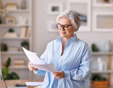 Mature businesswoman reading documents in home officeの写真素材