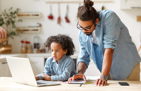 young ethnic father helps his son with homework while studying online on a laptop at homeの写真素材