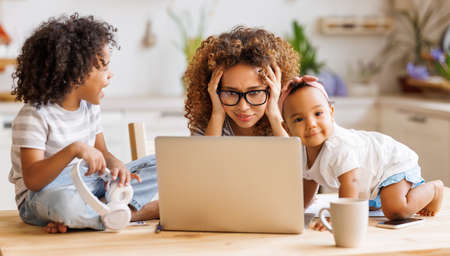 Young irritated African-American mother freelancer trying to work while working remotely with kidsの写真素材