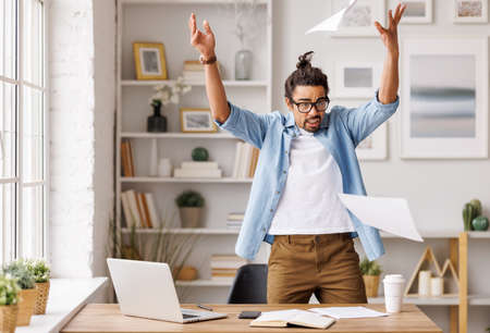 Furious black businessman throwing papers in home officeの写真素材