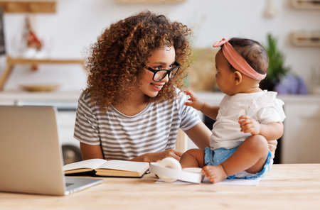 Freelance and motherhood. Happy young african american woman working remotely with cute baby girlの写真素材