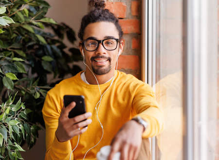 Black man listening to music near windowの写真素材