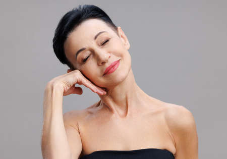 Middle aged woman touching face gainst gray backgroundの写真素材