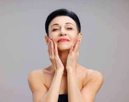 Middle aged woman touching face gainst gray backgroundの写真素材