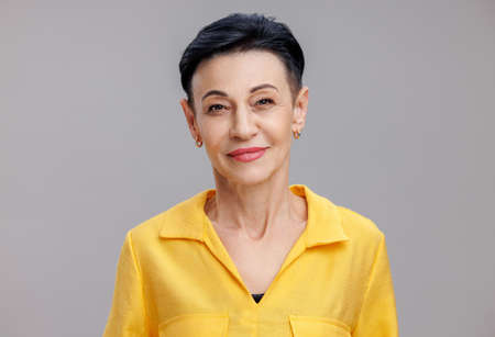 Smart mature female looking at camera against gray backgroundの写真素材