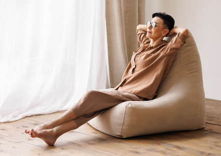 Relaxed mature female chilling near window at homeの写真素材