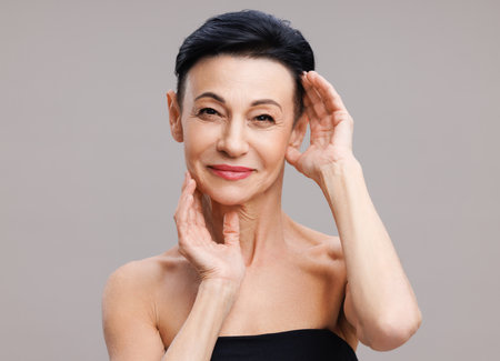 Middle aged woman touching face against gray backgroundの写真素材