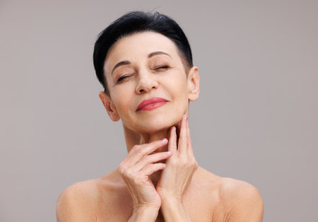 Middle aged woman touching face against gray backgroundの写真素材