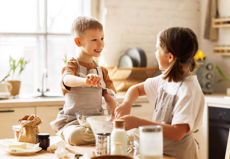 Happy children brother and sister making dough and cooking together in kitchenの写真素材