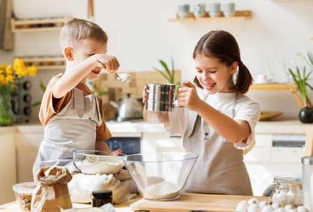 Happy children brother and sister making dough and cooking together in kitchenの写真素材